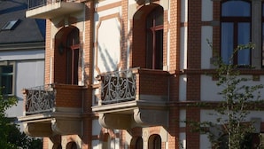 Een meerlaags gebouw met een bakstenen gevel, sierlijke ijzeren balkonnetjes en rondboogvensters.