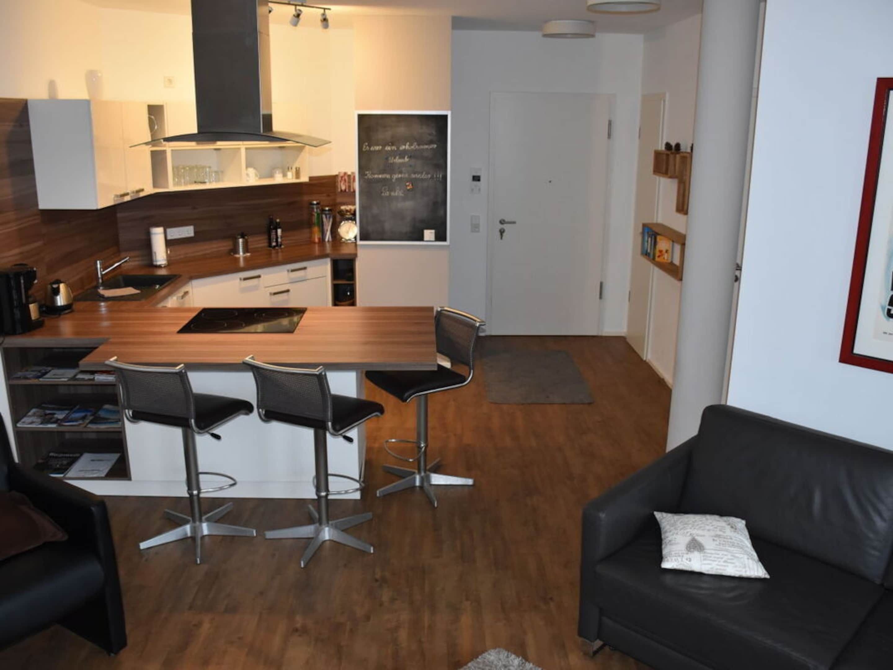 A modern kitchen with a central island, bar stools, a black leather sofa, and a framed picture on the wall.