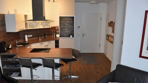A modern kitchen with a central island, bar stools, a black leather sofa, and a framed picture on the wall. - Charming Apaartment in Bremerhaven (Bremerhaven)