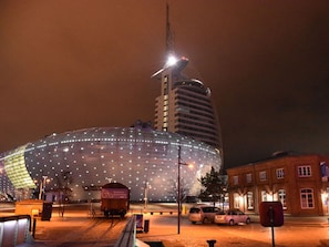 Ein großes, beleuchtetes Gebäude mit einer markanten, geschwungenen Außenfassade bei Nacht.