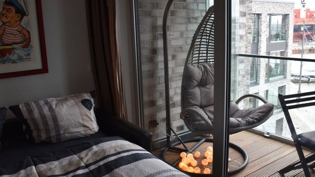 A modern room with a bed, a hanging chair, and a view of the city through large windows. - Charming Apaartment in Bremerhaven (Bremerhaven)