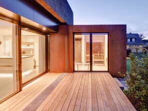 A modern house with a wooden deck, large sliding glass doors, and a visible kitchen area. - Seestuck Prerow (Ostseebad Prerow)