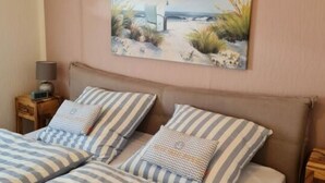 A bedroom with two beds, a nightstand with a lamp, and a painting of a beach scene on the wall. - Holiday Home Meerhuus (Butjadingen)