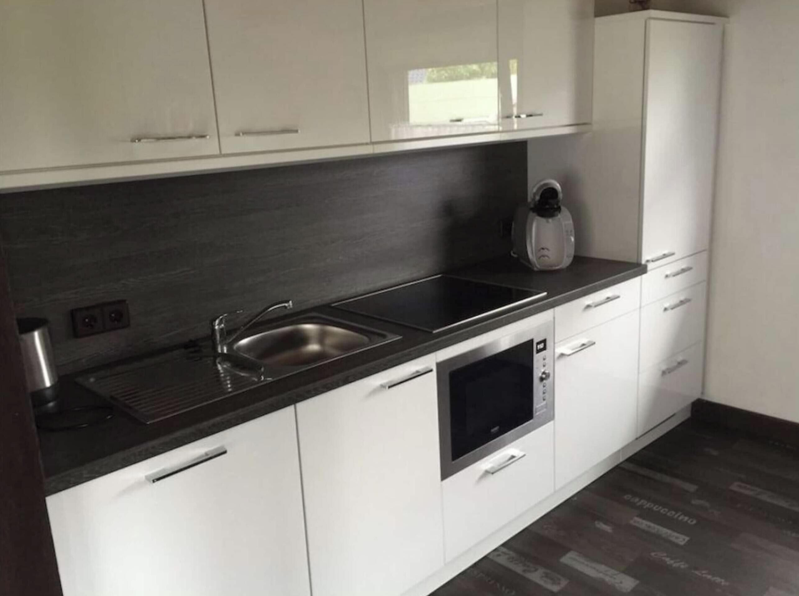 A modern kitchen with white cabinets, a stainless steel sink, a built-in oven, and a coffee maker.