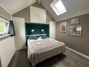 Un dormitorio con cama, dos lámparas de noche, una ventana con cortinas, un tragaluz y dos cuadros en la pared.
