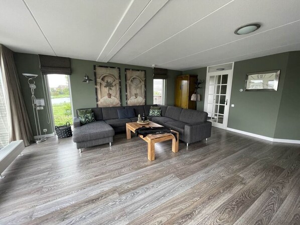 Un salón amplio con un sofá seccional gris, una mesa de centro de madera y un gran ventanal con vistas al exterior.