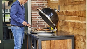 A person grilling meat on an outdoor barbecue with a brick wall and wooden paneling in the background. - Luxurious Holiday Home With Sauna in Limburg (Roggel)