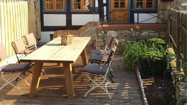 Ein traditionelles Fachwerkhäuschen mit einer Holzterrasse, Sitzgelegenheiten im Freien und Steinmauern.