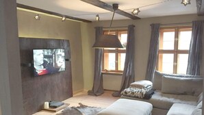 Ein Wohnzimmer mit an der Wand montiertem Fernseher, Deckenventilator, einer Couch und einem Fenster mit Vorhängen.