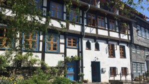Ein traditionelles Fachwerkhäuschen mit zahlreichen Fenstern und einer Steinwand davor.