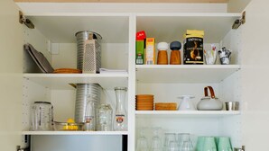 Una cocina con armarios blancos, estantes con utensilios de cocina y una tabla de cortar de madera.