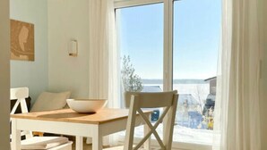 Un comedor con mesa y sillas de madera, una lámpara colgante y vistas amplias a través de grandes ventanales.
