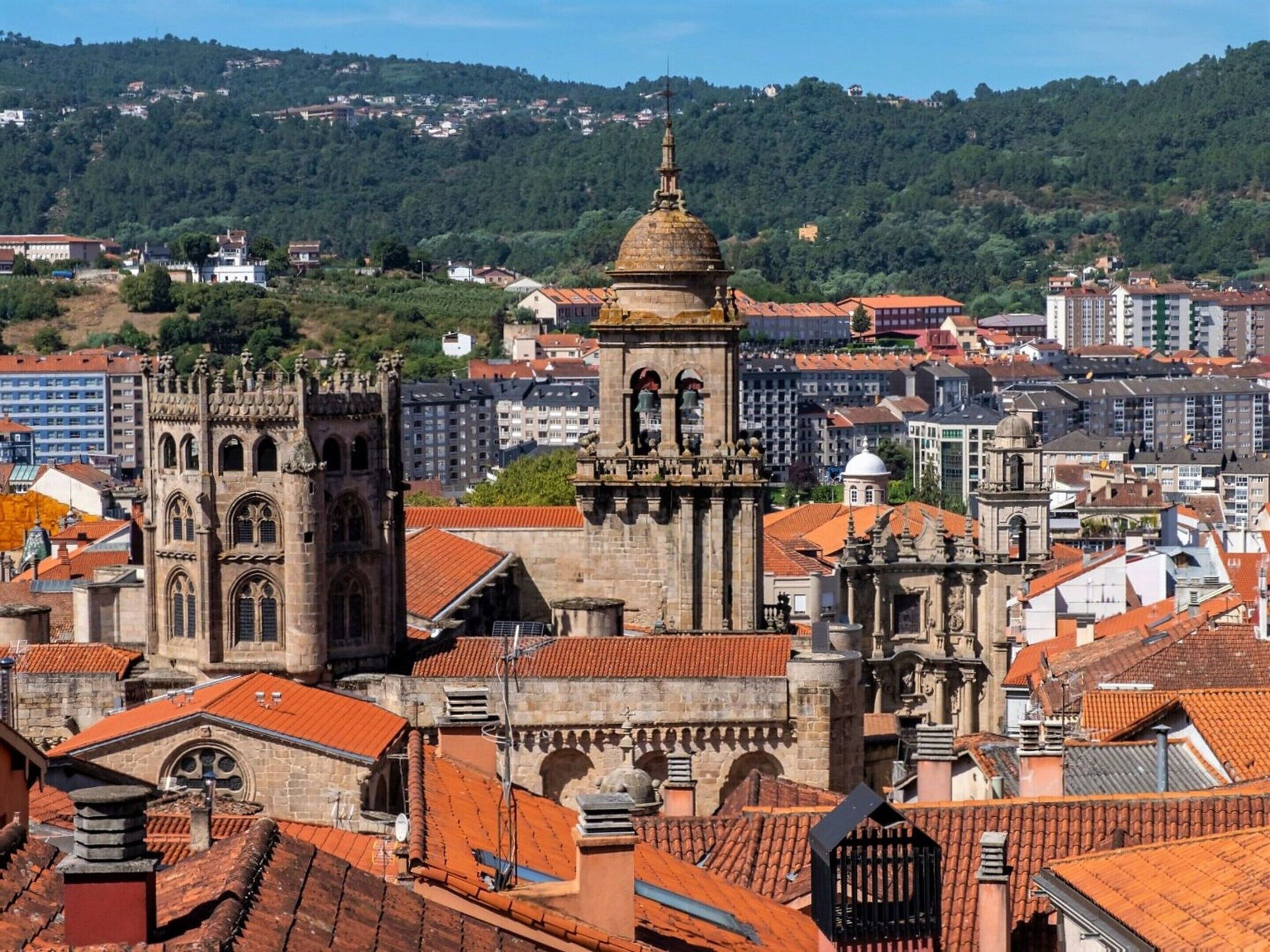 Una iglesia histórica con una destacada torre campanario y cúpula, rodeada de edificios tradicionales con tejados de tejas rojas.