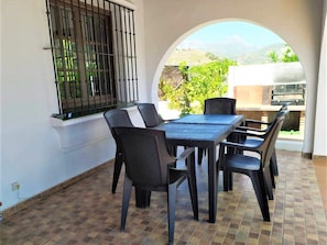 Un patio con mesa y sillas, una ventana con rejas y vistas a la vegetación y montañas.