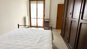 A bedroom with a bed, a radiator, a sliding glass door, a wardrobe, and a stack of books. - P028 - Porto Recanati, comfortable two-room apartment a few minutes from the bea (Porto Recanati)