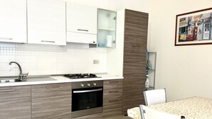 A modern kitchen with white cabinets, a gas stove, an oven, and a dining area with a table and chairs. - P028 - Porto Recanati, comfortable two-room apartment a few minutes from the bea (Porto Recanati)