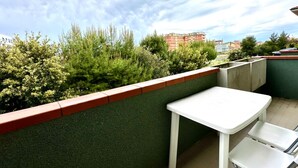 A balcony with a white table and chairs, surrounded by greenery and a red building in the background. - P028 - Porto Recanati, comfortable two-room apartment a few minutes from the bea (Porto Recanati)