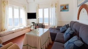 A living room with a sofa, a table, and a TV. There are windows with curtains and a painting on the wall. - Belvilla by OYO Chalet Corralete (Nijar)
