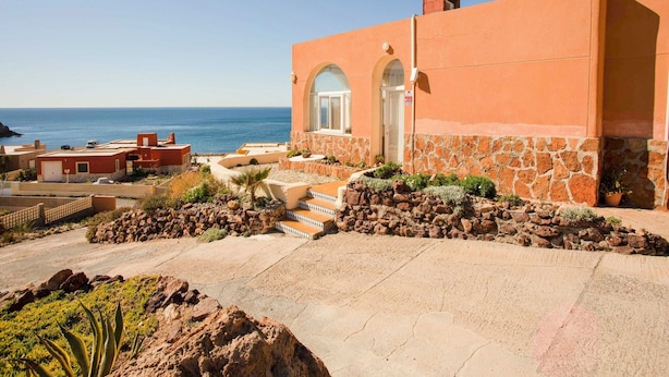 A coastal building with a stone facade, a large arched entrance, and a view of the sea. - Belvilla by OYO Chalet Corralete (Nijar)