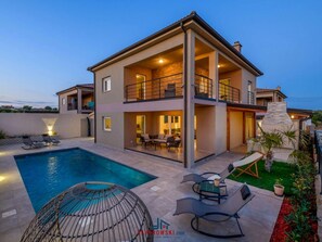Une maison à deux étages dotée d’une piscine, d’un espace salon extérieur et d’une cheminée en pierre.