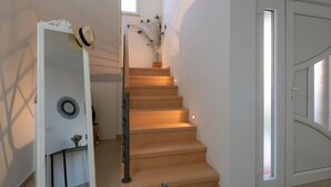 Un escalier avec des marches en bois et une rampe en verre, menant à un palier agrémenté d’un miroir décoratif et d’un vase contenant des plantes séchées.