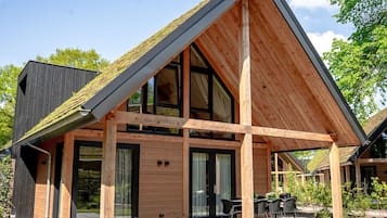 Una casa moderna con techo inclinado, ventanas amplias y un patio con mobiliario exterior.