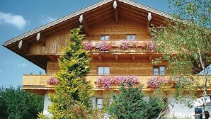 Un chalet en bois doté de balcons ornés de fleurs, entouré de verdure.