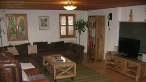 Un salon chaleureux avec un canapé en cuir marron, une table basse en bois, une bibliothèque et un téléviseur.
