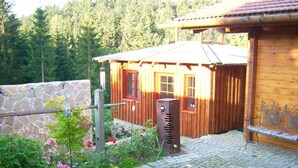 Une cabane en bois avec un mur en pierre, un banc en métal et un jardin agrémenté de fleurs et d’arbustes.