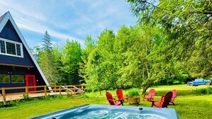 Un jacuzzi en un patio trasero con terraza de madera, rodeado de césped verde y árboles.