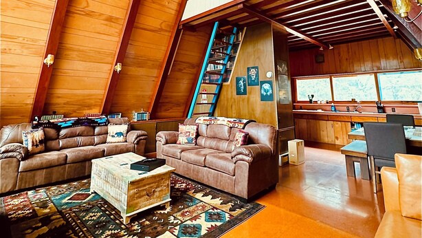 Un loft amplio con techos altos, interior de madera, un conjunto de sofás, un comedor y una escalera.