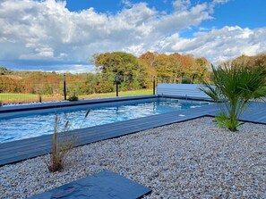 Relax by the pool surrounded by lush trees and a wooden deck.