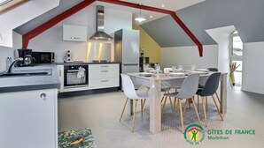 Una cocina moderna con comedor, que cuenta con una isla central, armarios blancos y un techo con vigas rojas.