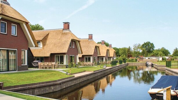 A canal-side property with thatched-roof houses, a narrow waterway, and a docked boat. - Villa in Friesland With Waterfront Jetty (Idskenhuizen)