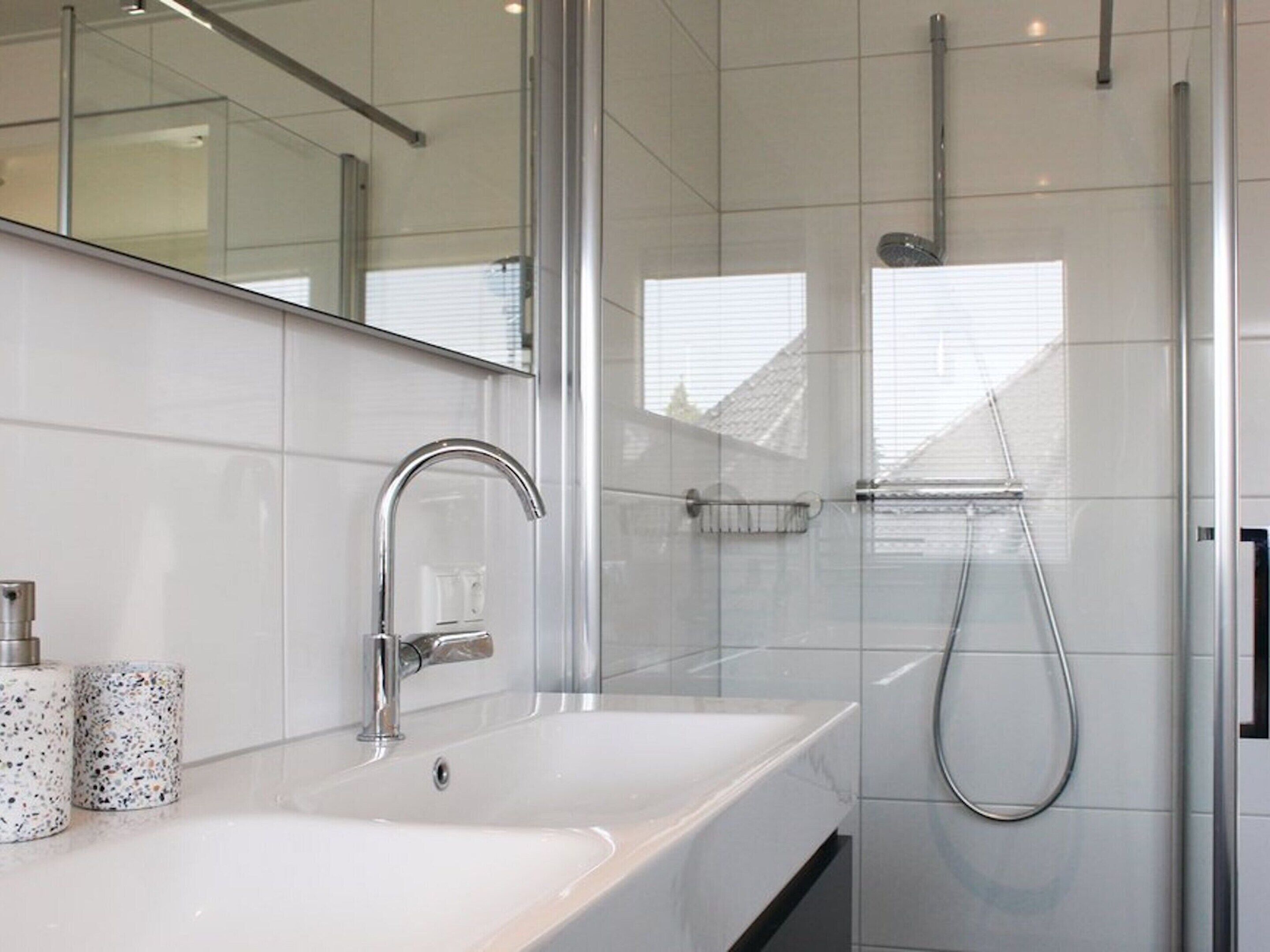 A modern bathroom with a large mirror, a sink, and a shower.