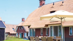 A row of houses with thatched roofs, a patio with a table and chairs, and a clear sky. - Villa in Friesland With Waterfront Jetty (Idskenhuizen)