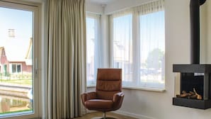 A room with a large window, a brown leather chair, and a black fireplace. - Villa in Friesland With Waterfront Jetty (Idskenhuizen)