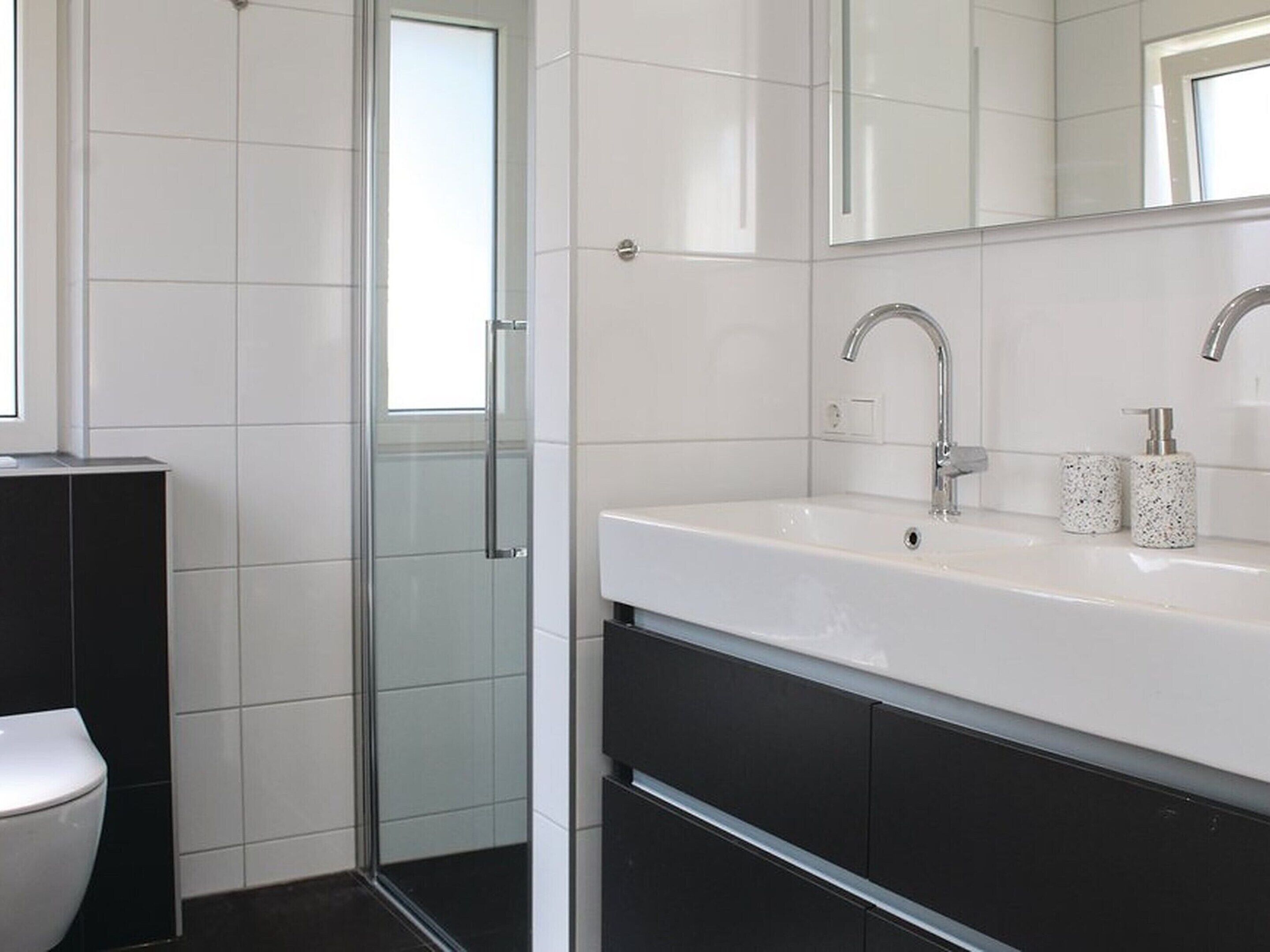 A modern bathroom with a glass shower enclosure, a white sink with a silver faucet, and a black cabinet below.
