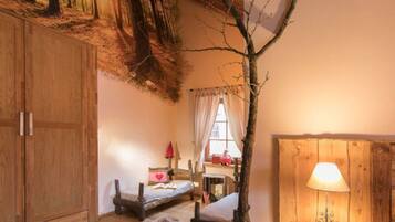 Ein gemütliches Zimmer mit Holzboden, einem Bett, einem kleinen Tisch mit Lampe und einem an der Wand befestigten Regal.