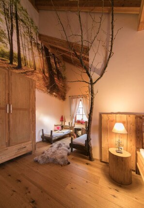 A cozy room with a wooden floor, a bed, a small table with a lamp, and a wall-mounted shelf.