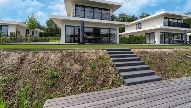 A modern two-story house with a flat roof, large windows, and a balcony.