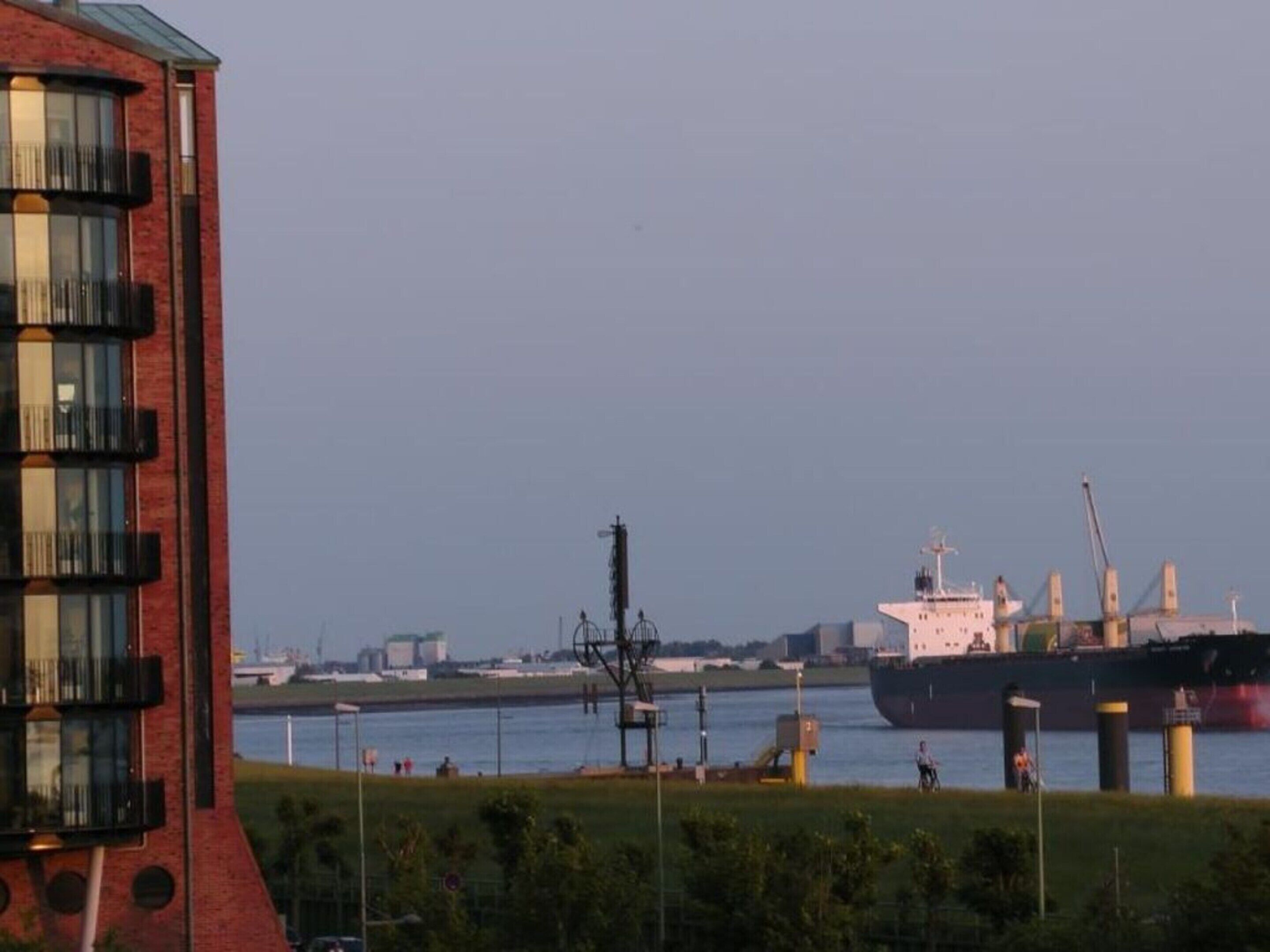Ein großes Frachtschiff liegt im Hafen vor einem Gebäude.