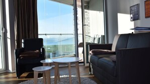 A modern living room with a sofa, a chair, a small table, and a view through a glass door to the outside. - Apartment Newport Weser (Bremerhaven)