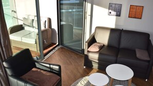 A modern living room with a leather sofa, a glass door leading to a balcony, and a small white table. - Apartment Newport Weser (Bremerhaven)