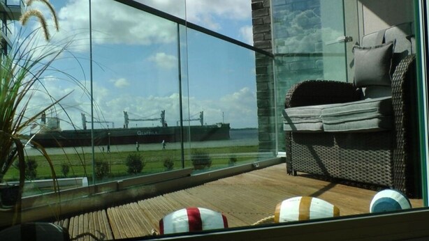 A balcony with a view of a ship and a grassy area. - Apartment Newport Weser (Bremerhaven)