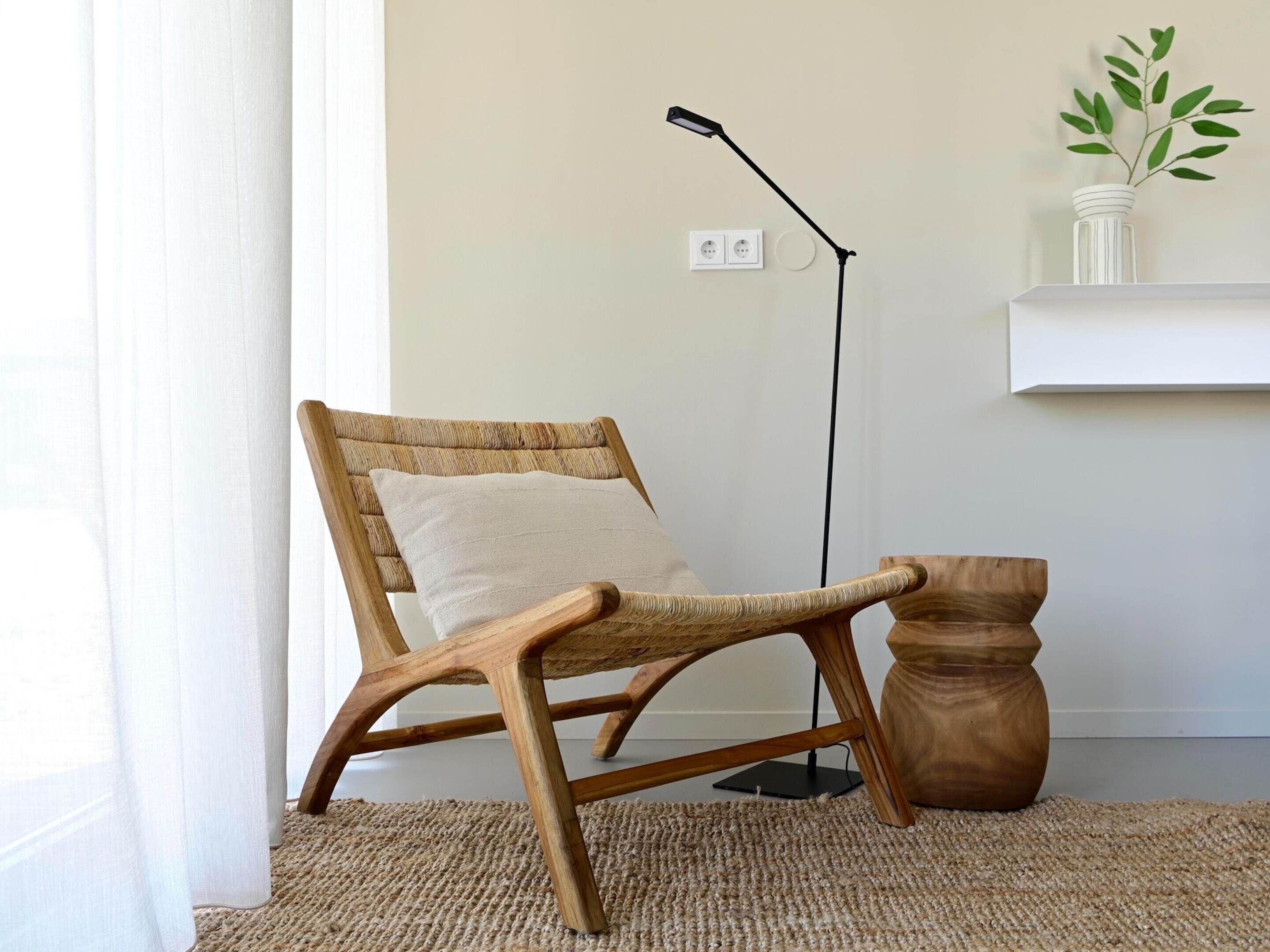 A wooden chair with a woven backrest and a cushion, a floor lamp, and a small wooden table.