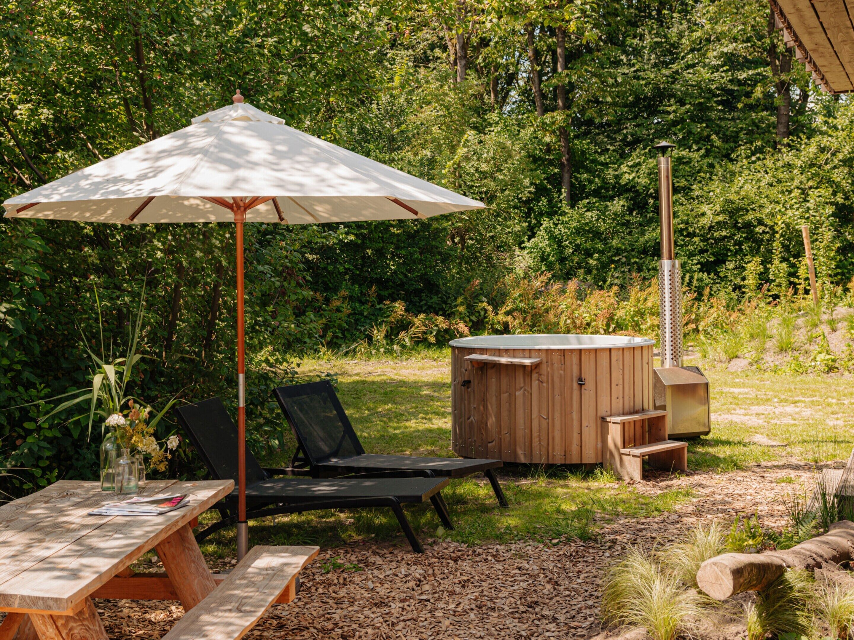 An outdoor seating area with a wooden table, two black lounge chairs, and a white umbrella.