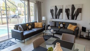 En moderne stue med sofa, sofabord og lænestole, en lampe og abstrakt kunst på væggen.