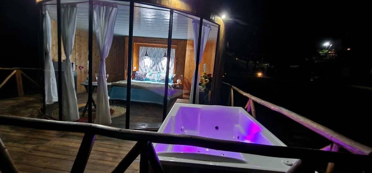 A wooden deck with a hot tub and a glass-enclosed room with curtains.