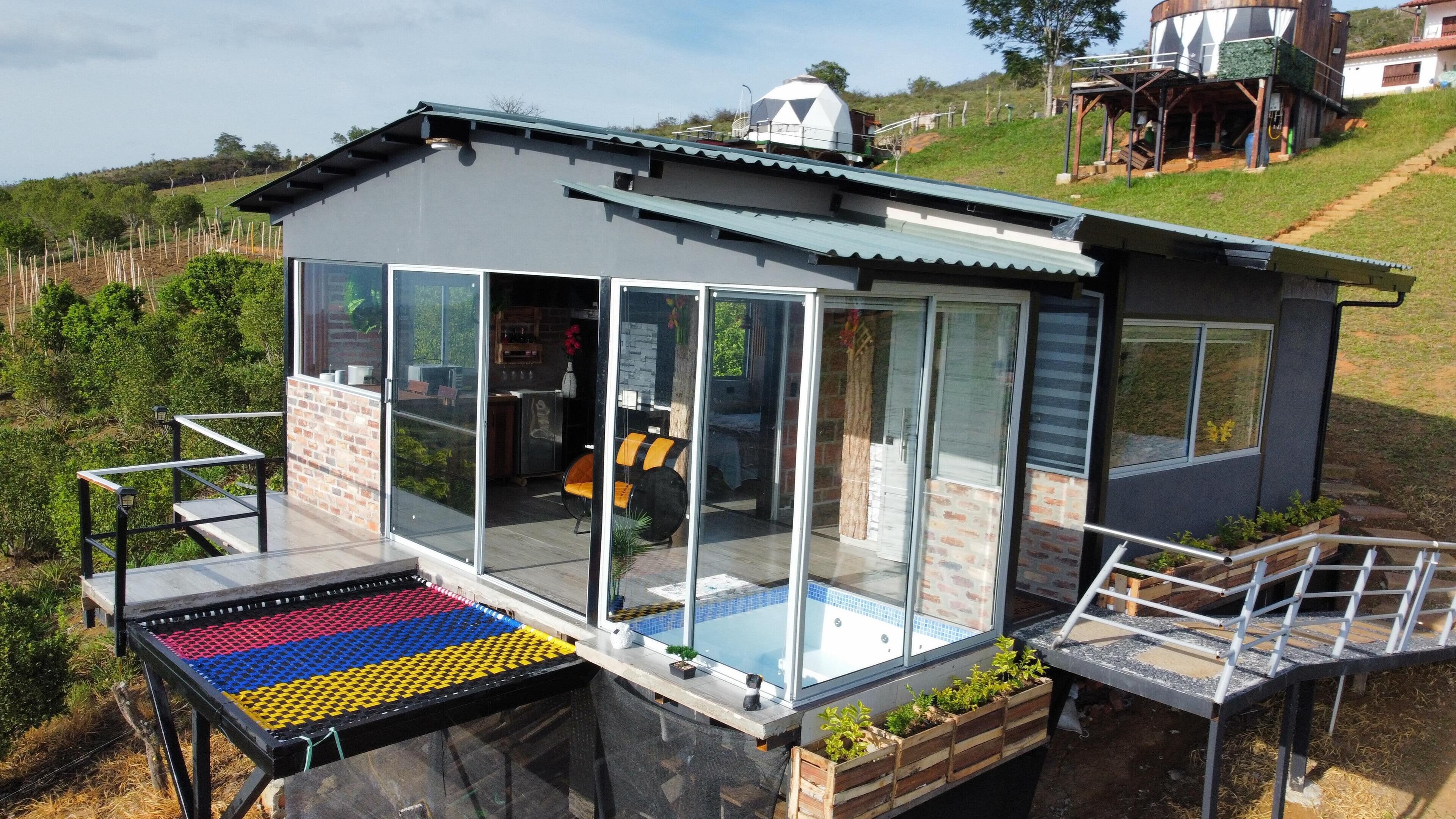 A modern house with a glass entrance, a small outdoor seating area, and a view of the surrounding landscape.